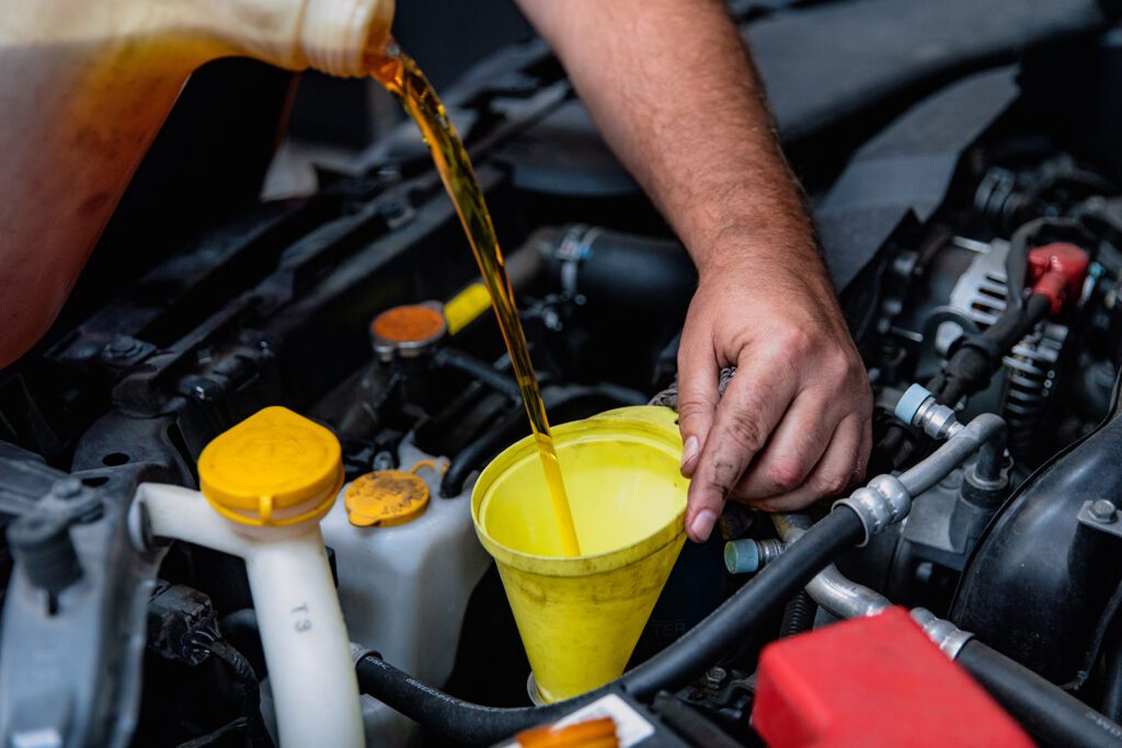 adding coolant to the Engine with a Yellow Pouring cup